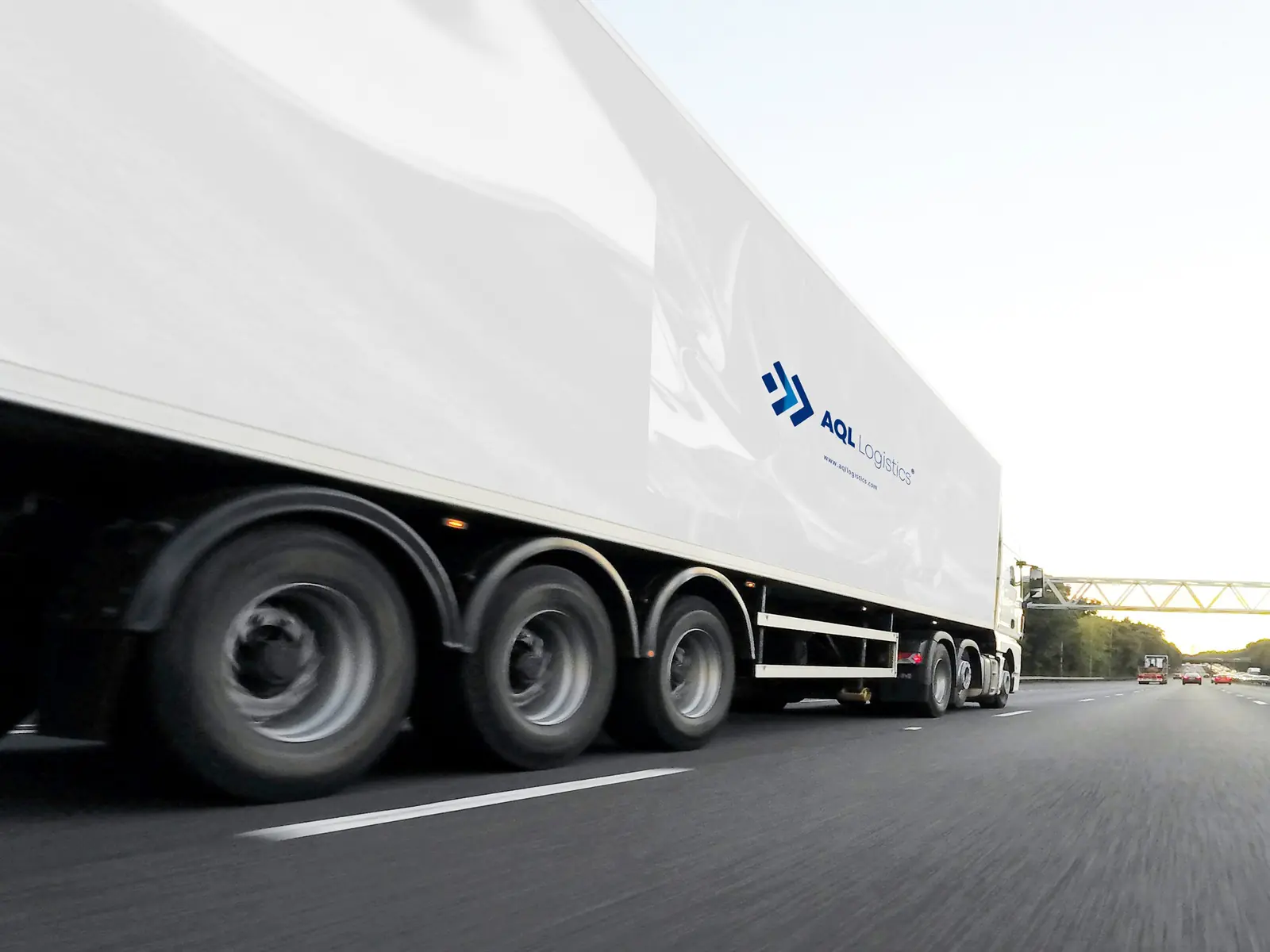 Tractocamión de AQL Logistics con caja refrigerada rotulada en autopista