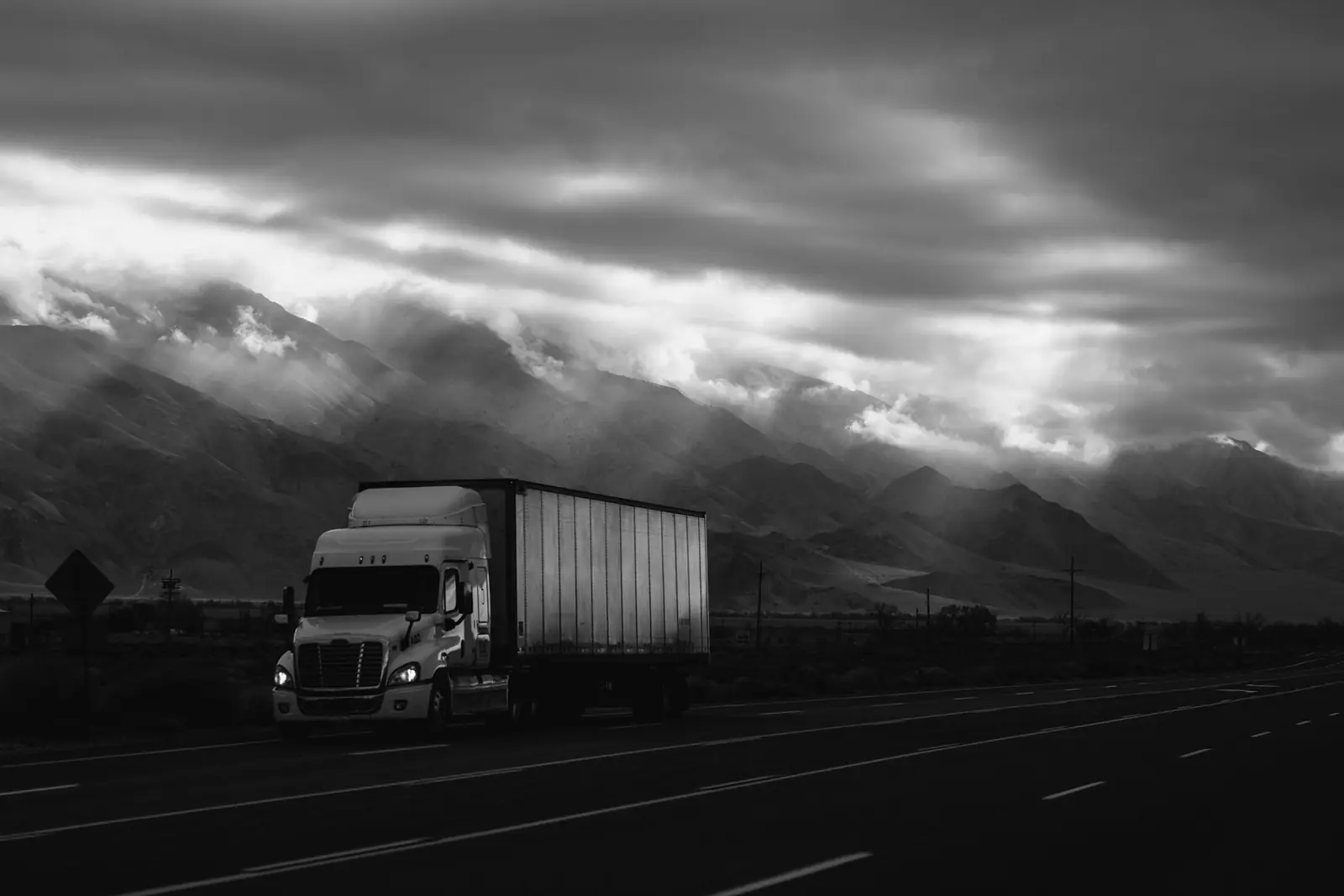 Tractocamión en carretera con montañas al fondo, en blanco y negro